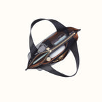 An overhead view of a black leather shoulder bag with its zipper open, showing its brown interior lining and compartments filled with accessories, on a solid off-white background.