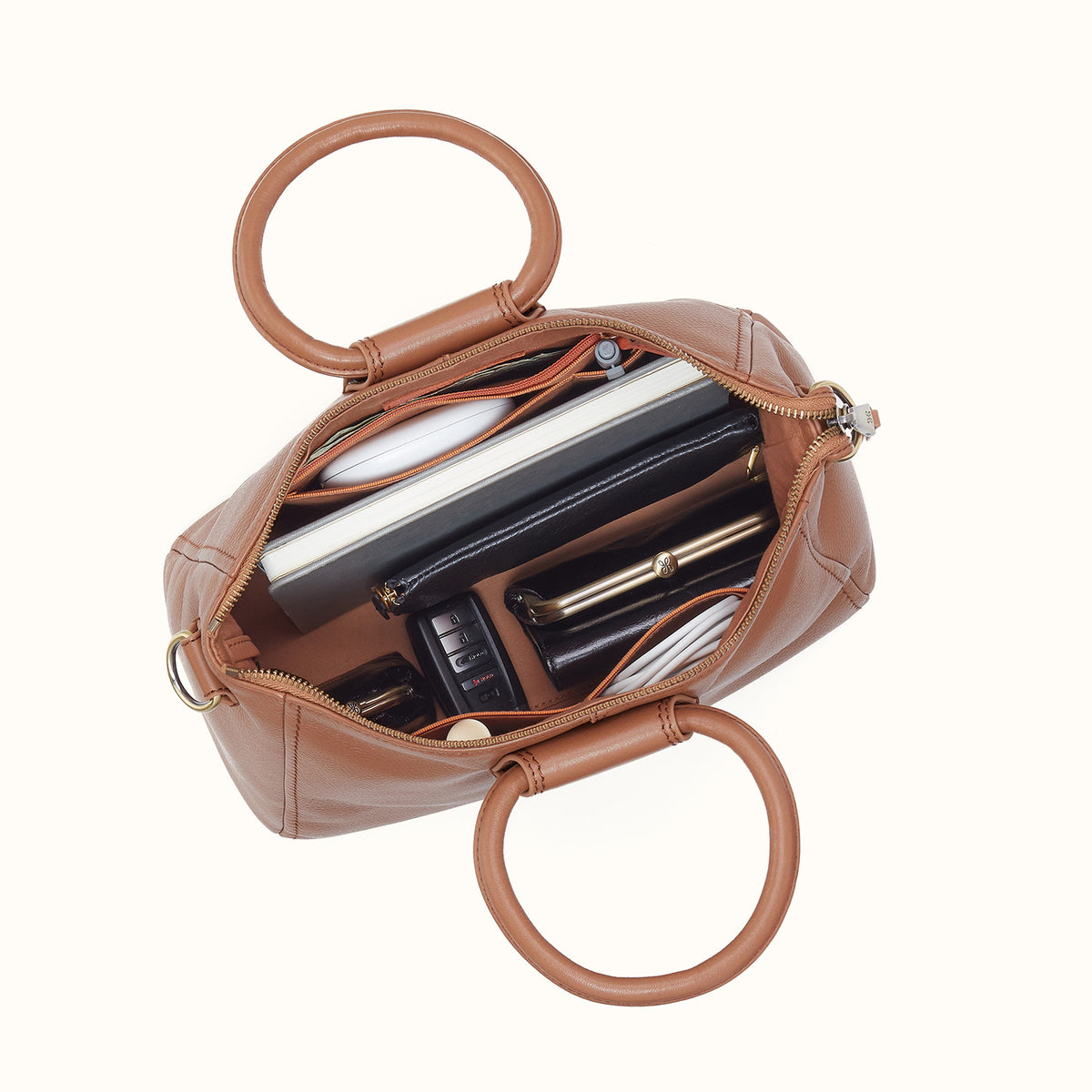 Brown handbag with circular handles, open to reveal its contents on a white background