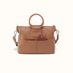 A tan pebbled leather handbag with a top handle, a detachable shoulder strap, and a front slip pocket holding a burgundy phone, shown against a plain off-white background.