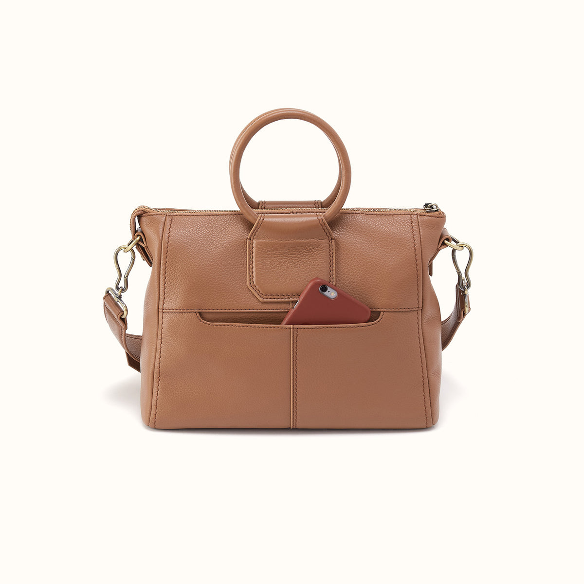 A tan pebbled leather handbag with a top handle, a detachable shoulder strap, and a front slip pocket holding a burgundy phone, shown against a plain off-white background.