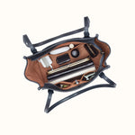 An overhead view of an open black leather handbag with a brown interior, shown packed with various cosmetics and accessories against a plain off-white background.