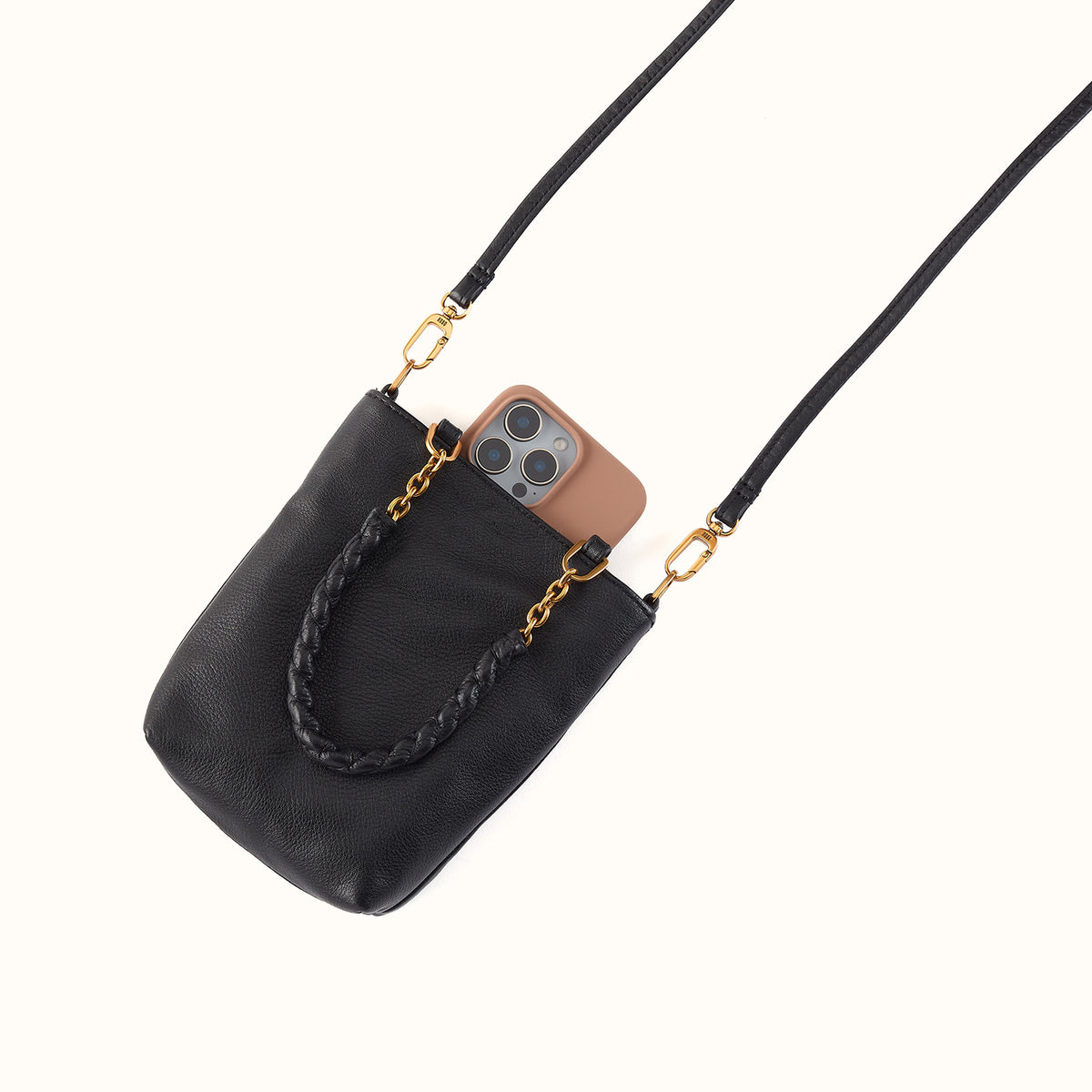Black crossbody bag with gold chain detail holding a phone on a light gray background