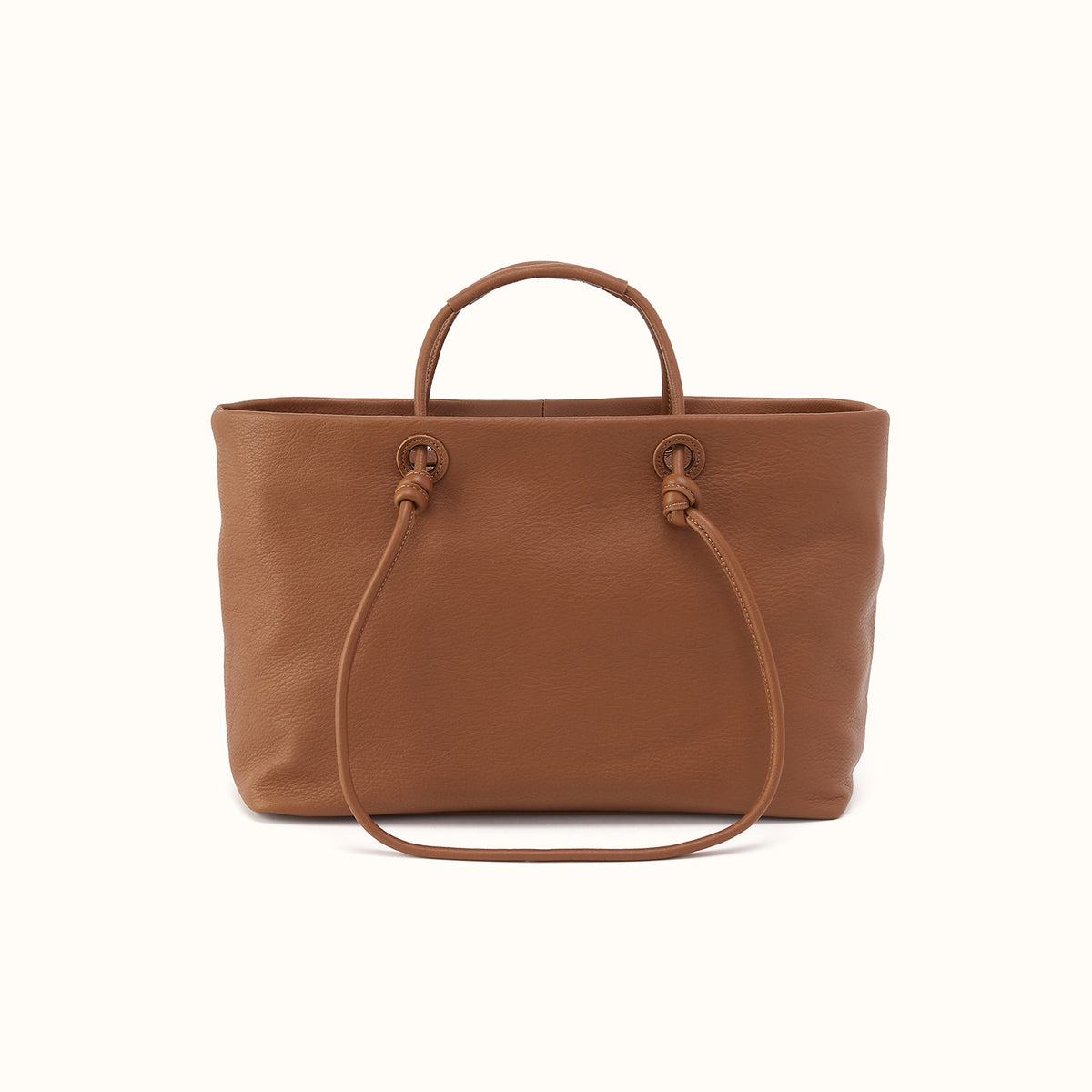 A brown pebbled leather tote bag with two top handles and a long shoulder strap, photographed against a clean off-white background.