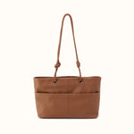 A medium brown leather tote bag with a single shoulder strap featuring knotted details at the top, set against a plain off-white background.