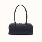 A black leather handbag with double top handles and gold-tone hardware, photographed against a clean off-white background.