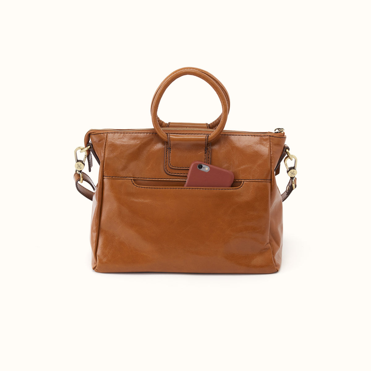 A brown leather handbag with a top handle, a front pocket, and a small burgundy card tucked into the pocket, shown against a plain off-white background.